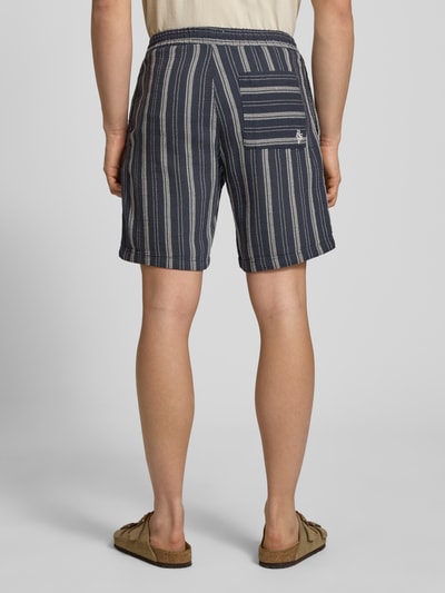 Mężczyzna nosi Shorts mit elastischem Bund und Logo-Detail von REVIEW, granatowy bawełniany materiał w paski, krój regular fit, Szerokość w rozmiarze M: 42 cm, długość nogawki od wewnątrz: 20 cm, widok całej sylwetki z tyłu.