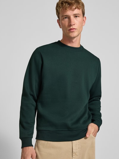 Männermodel trägt Regular Fit Sweatshirt mit Baumwoll-Anteil Modell 'Bradley' von JACK & JONES in Dunkelgrün, Nahaufnahme Oberkörper. Material-Mix, Rundhalsausschnitt, Langarm, gerippte Abschlüsse, Logo-Label.