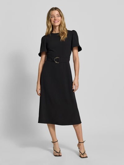 Frauenmodel trägt Cocktailkleid mit Gürtel und Rundhalsausschnitt von Rinascimento in Schwarz, Material-Mix mit Stretch-Anteil, Taillierter Schnitt, Midikleid, rückseitiger Reißverschluss, Rückenlänge 36 cm, Brustweite 40 cm, Ärmellänge 28 cm, Ganzkörperansicht von vorne.
