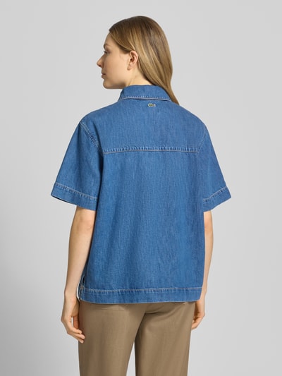 Modelka nosi Regular Fit Jeansbluse aus reiner Baumwolle von Lacoste, tkanina stylizowana na denim, krój regular fit, kołnierzyk koszulowy, wyhaftowane logo, szwy w kontrastowym kolorze, listwa guzikowa, krótki rękaw, wykończenie z bocznymi rozcięciami, brustasza, bawełna, widok całej sylwetki od tyłu.