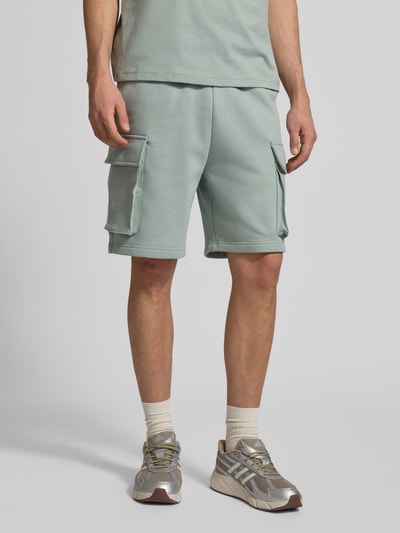 Männermodel trägt Sweatshorts mit Cargotaschen und Logo von CHAMPION in Mintgrün, Baumwoll-Mix, Relaxed Fit, Nahaufnahme Oberkörper bis Knie.