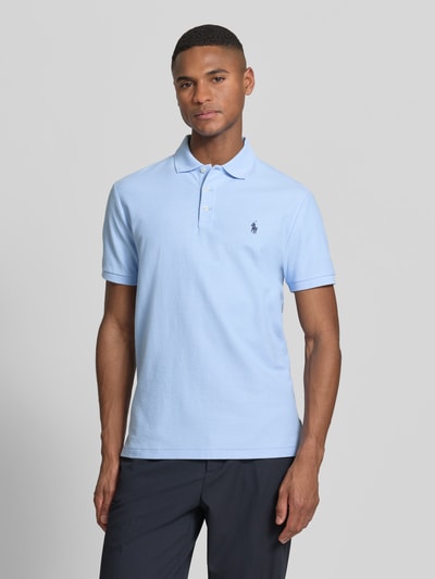 Männermodel trägt Slim Fit Poloshirt aus reiner Baumwolle von Polo Ralph Lauren in effen lichtblauw piqué, logodetail, korte mouw, polokraag, V-hals, knoopsluiting, mouwboord en rompzoom met zijsplitten, asymmetrisch, puur katoen. Ganzkörperansicht von vorne.
