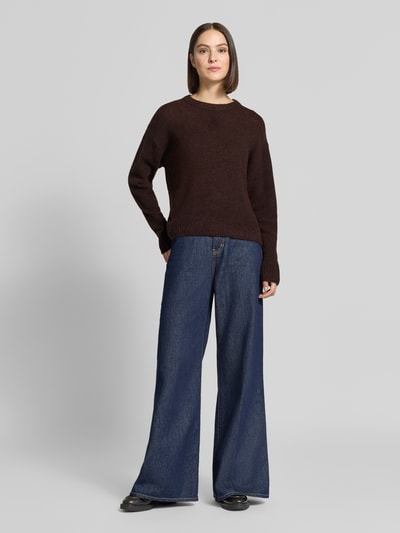 Modelka nosi sweter z dzianiny Relaxed Fit Strickpullover aus Woll-Mix mit Alpaka-Anteil od FREE/QUENT, mieszanka wełny z alpaką, okrągły dekolt, prążkowane wykończenia, długość tyłu w rozmiarze S 58 cm, długość rękawów 56 cm, kolor brązowy, gładka tekstura, szerokie spodnie jeansowe, widok całej sylwetki z przodu.