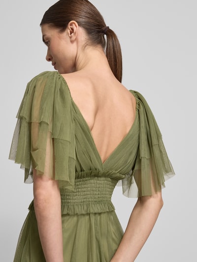 Frauenmodel trägt Maxikleid mit V-Ausschnitt und Taillenband von LACE & BEADS aus grünem Tüll mit tailliertem Schnitt, Detailaufnahme Rückansicht. Rückenlänge bei Größe S: 152 cm, Brustweite bei Größe S: 31 cm, Ärmellänge bei Größe S: 29 cm.