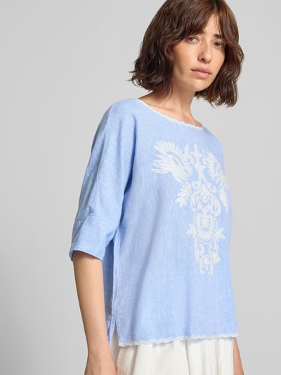 Modelka kobieca ma na sobie Blusenshirt mit Leinen-Anteil und Motiv-Stitching od Christian Berg Woman, mieszanka wiskozy i lnu, krój loose fit, dekolt w łódkę z kontrastową lamówką, wyhaftowany motyw, długość tyłu 55 cm, długość rękawów 34 cm, jasnoniebieski kolor, widoczne delikatne faktury, szeroki haft z przodu, półmatowy materiał, całkowity widok z przodu.