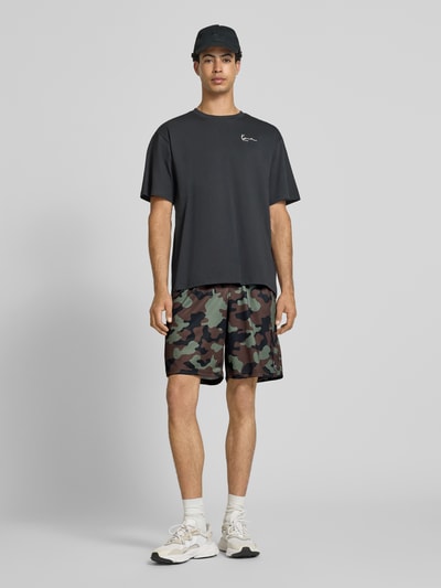 Männermodel trägt Regular Fit Shorts mit elastischem Bund von KARL KANI mit Strukturmuster, Logo-Stitching, Tarnfarbenmuster, Ganzkörperansicht von vorne. Bundweite 38 cm, Innenbeinlänge 22 cm, Größe M.