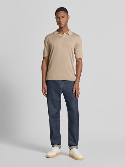 Męski model nosi Slim Fit Poloshirt aus Lyocell-Baumwoll-Mix od OLYMP Level Five, krój slim fit, kołnierzyk polo, krótki rękaw, mieszanka lyocellu i bawełny, długość tyłu w rozmiarze M: 68 cm, kolor beżowy, granatowe spodnie, jasne buty, gładka tekstura, całkowity widok z przodu