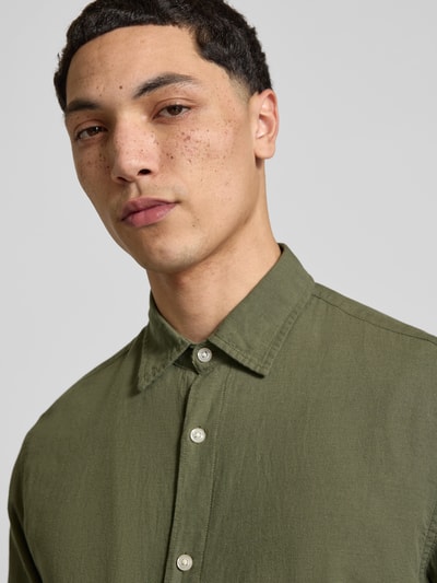 Męski model nosi Regular Fit Freizeithemd mit Kentkragen Modell 'BREEZE' von Jack & Jones, mieszanka bawełny i lnu, listwa guzikowa, krój regular fit, długość tyłu w rozmiarze M 73 cm, szerokość ramion w rozmiarze M 48 cm, długość rękawów w rozmiarze M 63 cm, oliwkowa z fakturą, zbliżenie na górną część torsu