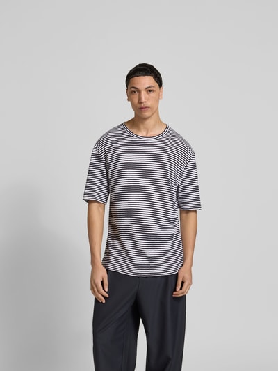 Männermodel trägt Regular Fit T-Shirt aus Leinen-Mix von Officine Générale, schwarz-weiß gestreift, Halbarm, Ganzkörperansicht von vorne.