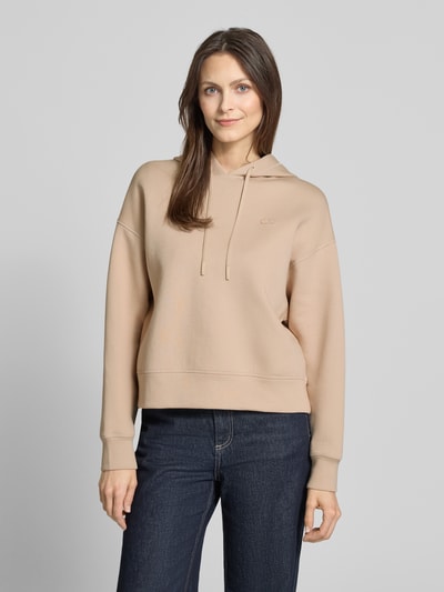 Frauenmodel trägt Oversized Hoodie aus Baumwoll-Mix von Lacoste Sport in Beige, unifarben, langarm, Logo-Applikation, Nahaufnahme Oberkörper.