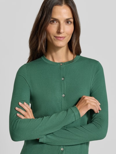 Vrouwenmodel draagt Regular fit gebreid jack uit viscosemix met geschulpte zoom van Christian Berg Woman, groene kleur, ribboorden, knoopsluiting, lange mouw, ruglengte maat S 56 cm, mouwlengte maat S 61 cm, Nahaufnahme Oberkörper.