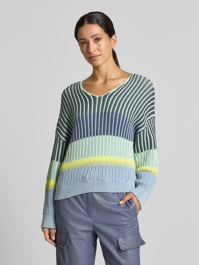 Frauenmodel trägt Oversized Strickpullover mit V-Ausschnitt von Marc Cain im Baumwoll-Mix, gestreifte Blautöne, gelbe Akzente, gerippte Abschlüsse, Ganzkörperansicht von vorne.