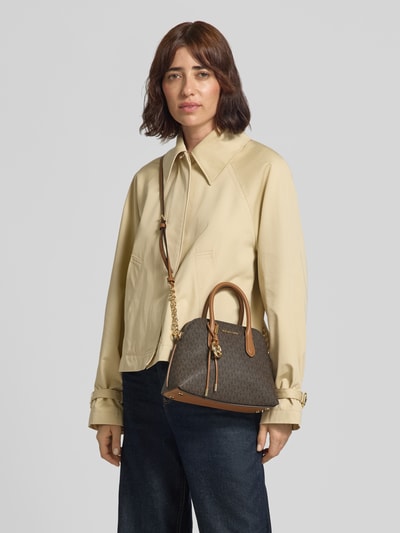 Kobiece model nosi torebkę z nadrukiem z logo na całej powierzchni MICHAEL Michael Kors model 'Freddie', efekt łańcuszka, aplikacja z logo, Główna przegroda z zamkiem błyskawicznym, Szerokość w rozmiarze 1: 26 cm, Długość w rozmiarze 1: 21 cm, Głębokość w rozmiarze 1: 10 cm, Długość paska na ramię w rozmiarze 1: 120 cm, kolor brązowy, Ganzkörperansicht von vorne.
