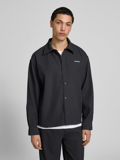 Męski model nosi Regular Fit Freizeithemd mit Kentkragen und Label-Stitching od Pegador, czarne, tekstura prążkowana, krój regular fit z domieszką stretchu, długość pleców 68 cm, szerokość w rozmiarze M 50 cm, długość rękawa 60 cm, widok całej sylwetki z przodu.