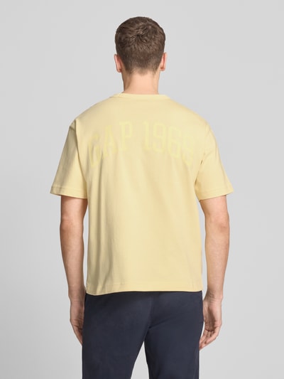 Mannelijk model draagt T-shirt met logo en ronde hals van GAP in lichtgeel, puur katoen, regular fit, ruglengte maat M 61 cm, geheelopname achteraan.