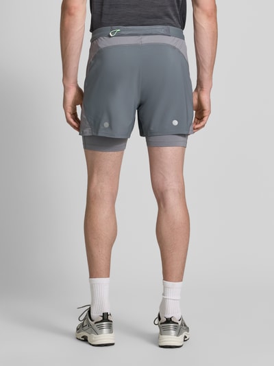 Męski model nosi Regular Fit Shorts mit integrierten Tights Model 'Road' od ASICS TIGER, szary kolor, detal z logo, elastyczny pas, krój regular fit, Szerokość w rozmiarze M: 38 cm, Długość wewnętrzna nogawki: 12 cm, całkowity widok od tyłu