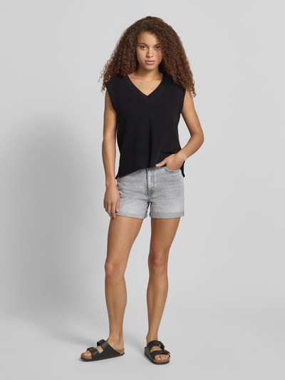 Modelka nosi szorty jeansowe High Waist Jeansshorts mit Umschlag Modell 'MONI' von Noisy May z mieszanki bawełny i elastanu, wpuszczane kieszenie, brzeg, szerokość w rozmiarze S: 35 cm, długość wewnętrzna nogawki w rozmiarze S: 9 cm, jasnoszara struktura, cała sylwetka z przodu.