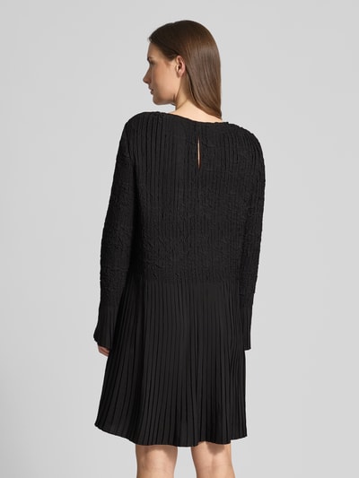 Vrouwenmodel draagt Tailliertes Cocktailkleid mit Raffung-Optik Modell 'Doppar' van BOSS, zwart, structuur, mini, lange mouw, frill, keyhole rug, geheel achteraanzicht.