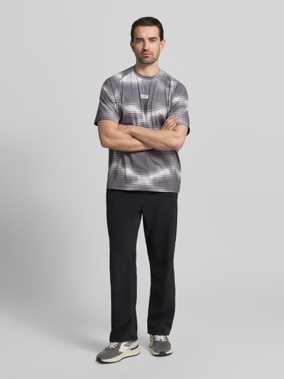 Männermodel trägt Regular Fit T-Shirt mit Logo-Applikation von EA7 Emporio Armani, elastischer Materialmix, Schwarz-Grau, Ganzkörperansicht von vorne.