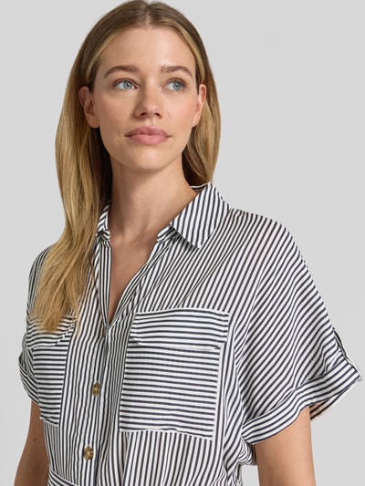 Kobiece model nosi Fließendes Freizeitkleid aus reiner Viskose Modell 'BUMPY' od Vero Moda, jednokolorowa popelina, dekolt w serek, listwa guzikowa, pas na plecach, krój luźny, długość mini, krótki rękaw, wykończenie: czysta wiskoza, zbliżenie na górną część ciała.
