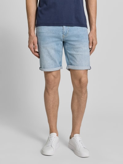 Männermodel trägt Slim Fit Jeansshorts aus Baumwoll-Mix Modell 'NAAILO' von Armedangels in Denim-Optik mit Label-Patch, 5-Pocket-Design, Gürtelschlaufen, Knopf- und Reißverschluss, Beinabschluss mit Umschlag, Ganzkörperansicht von vorne.