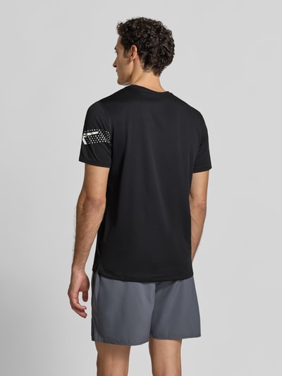 Męski model nosi t-shirt Regular Fit T-Shirt mit Label-Print Modell 'ICON' od ASICS TIGER, czarny z nadrukiem z logo, okrągły dekolt, Długość tyłu w rozmiarze M: 71 cm, Ganzkörperansicht Rückansicht.