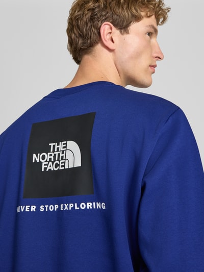 Männermodel trägt Regular Fit Hoodie mit Logo-Detail Modell "EVOLUTION BOX" von The North Face in Blau, Baumwoll-Mix, Nahaufnahme Rückansicht. Rückenlänge 62 cm, Ärmellänge 70 cm, Markenpatch und Schriftzug, elastische Abschlüsse, Kontext: Herren Hoodie.