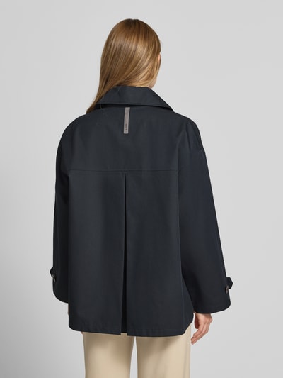 Männermodel trägt Trenchjacke mit Reverskragen Modell 'HEATHER' von G-LAB, prosty krój, czarny, guzik, długość tyłu 70 cm, szerokość ramion 48 cm, szerokość w rozmiarze S 52 cm, długość rękawa 51 cm, widok całej sylwetki z tyłu.
