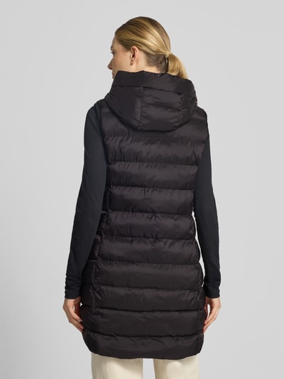 Vrouwenmodel draagt Regular Fit bodywarmer in stiksels van FUCHS SCHMITT, zwart met capuchon en steekzakken met ritssluiting, ruglengte 77 cm, schouderbreedte 41 cm, borstwijdte 51 cm, doorgestikte structuur, ganzebody van achteraanzicht.