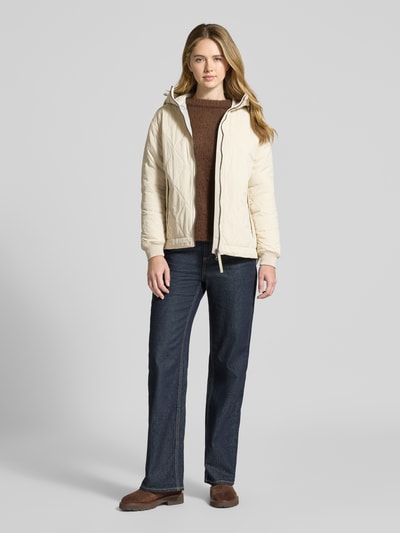Vrouwenmodel draagt gewatteerd jack met tweewegritssluiting van camel active, recht pasvorm, capuchon met tunnelkoord, steekzakken, elastische mouwboorden, kleur crème, materiaal met lichte structuur, ruglengte 71 cm, schouderbreedte 48 cm, borstwijdte 56 cm, mouwlengte 58 cm. Ganzekörperaanzicht van voren.