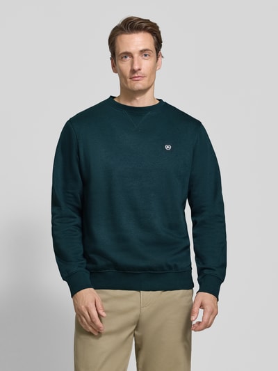 Männermodel trägt Regular Fit Sweatshirt aus Baumwoll-Mix von LERROS in Dunkelgrün mit Logo-Patch, Ganzkörperansicht von vorne.