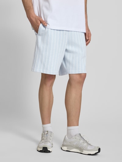 Męski model nosi szorty Straight Fit Shorts mit Strukturmuster Modell 'Forno' von Pegador z bawełny, fakturowany wzór, elastyczny pas, szerokość w rozmiarze M: 42 cm, długość wewnętrzna nogawki w rozmiarze M: 23 cm, jasnoniebiesko-biały, prosty krój; całkowity widok z przodu.