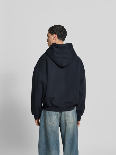 Männermodel trägt Regular Fit Hoodie mit Logo-Print von RHUDE in Dunkelblau, Reine Baumwolle, elastische Abschlüsse, Ganzkörperansicht Rückansicht. Rückenlänge bei Größe M: 65 cm, Känguru-Tasche.