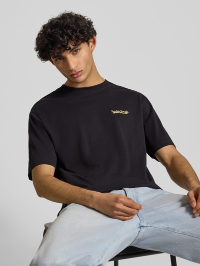 Männermodel trägt Relaxed Fit T-Shirt aus reiner Baumwolle Modell 'FRED DU MARTIN' von Only & Sons, unifarben schwarz, Motiv-Print, Feinripp, Ganzkörperansicht von vorne.