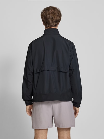 Männermodel trägt schwarze Regular Fit Jacke in Stehkragen Modell 'Fast Days' von New Balance, elastische Ärmelabschlüsse, Ganzkörperansicht Rückansicht.