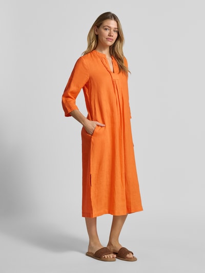 Frauenmodel trägt Tunikakleid aus Leinen mit 3/4-Arm von Emily Van den Bergh in Orange, Loose Fit, Midilänge, Ganzkörperansicht von vorne.