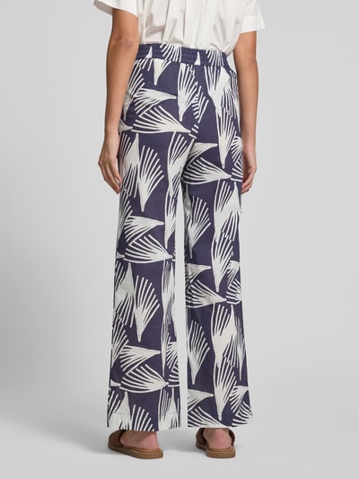 Frauenmodel trägt Wide Fit Stoffhose mit floralem Allover-Print Modell 'Lani' von GUIDO MARIA KRETSCHMER WOMAN in Dunkelblau und Weiß, aus reiner Baumwolle, elastischer Bund mit Tunnelzug, florales Muster, Ganzkörperansicht Rückansicht.