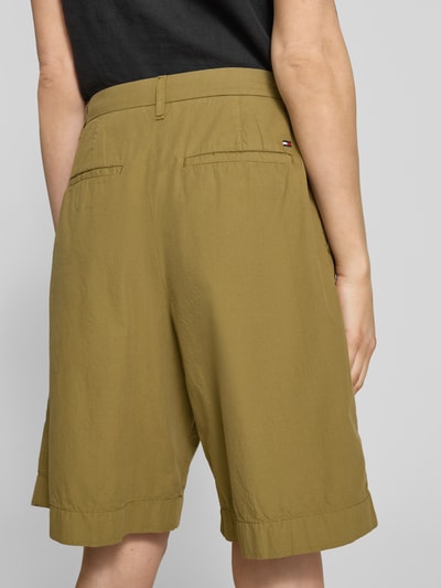 Frauenmodel trägt Relaxed Fit Bermuda aus reiner Baumwolle von Tommy Hilfiger in Olive mit Bundfalte und Logo-Stitching, Ganzkörperansicht Rückansicht