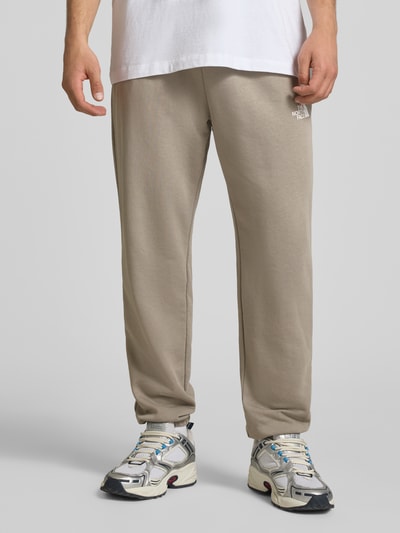 Männermodel trägt Sweatpants mit Logo-Print von The North Face, herren, Baumwoll-Mix, Slim-Fit, elastischer Bund mit Kordelzug, elastische Abschlüsse, beige Farbe, glatte Textur, Innenbeinlänge 70 cm bei Größe M, Ganzkörperansicht von vorne.