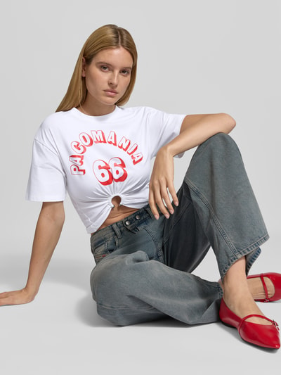 Frauenmodel trägt Cropped T-Shirt mit Zier-Detail von Rabanne, weiß mit rotem Statement-Print, Rundhalsausschnitt, Nahaufnahme Oberkörper.