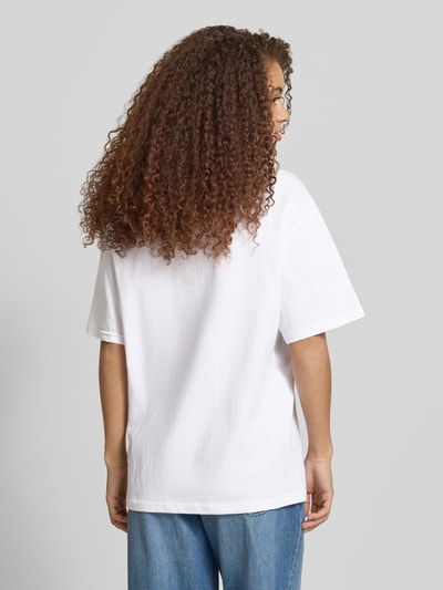 Frauenmodel trägt T-Shirt mit rückseitigem Motiv-Print von REVIEW aus Reine Baumwolle im Oversized-Stil mit Rundhalsausschnitt, Rückenlänge 68 cm bei Größe S, Weiß und Blau, Ganzkörperansicht Rückansicht.