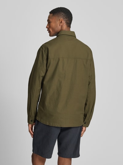 Männermodel trägt Regular Fit Hemdjacke aus reiner Baumwolle von camel active in Olivgrün, Struktur-Textur, Rückenansicht, Ganzkörperansicht Rückansicht. Rückenlänge bei Größe M: 74 cm, Schulterbreite bei Größe M: 44 cm, Brustweite bei Größe M: 53 cm, Ärmellänge bei Größe M: 66 cm, Umlegekragen, Durchgehende Knopfleiste, Langärmelig, Brusttaschen, Statement-Patch, Label-Detail.