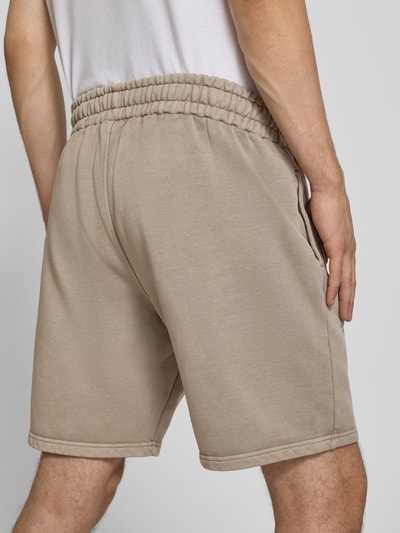 Männermodel trägt Regular Fit Sweatshorts mit Logo-Stitching von Pegador in Beige, Baumwoll-Mix, elastischer Bund, Ganzkörperansicht Rückansicht.