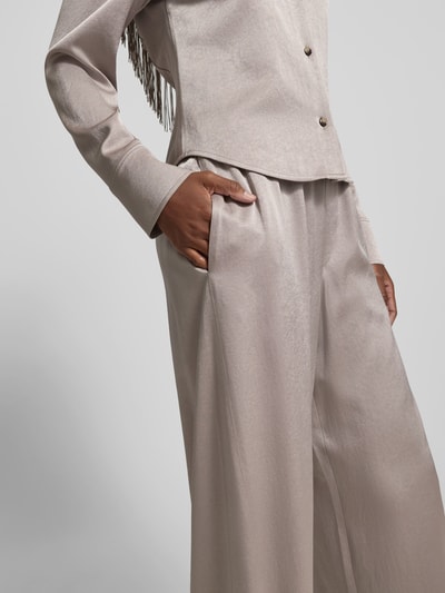 Vrouwenmodel draagt Stoffhose met elastischem Bund van Nanushka, beige fluweel, relaxed fit, siernaden, detailopname heup en bovenbeen.