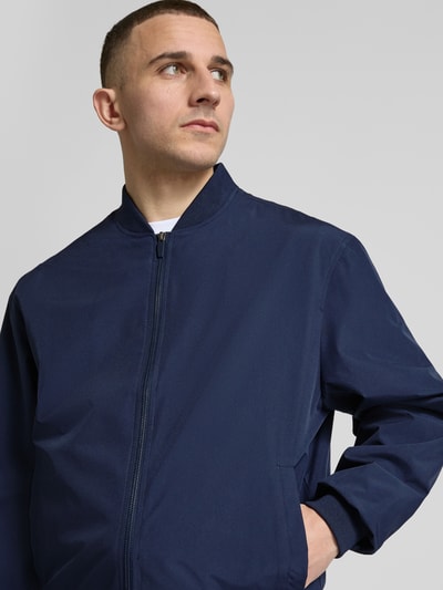 Männermodel trägt dunkelblaue Herren Bomberjacke mit Stehkragen Modell 'CHARGE' von Jack & Jones; Regular-Fit, Reißverschluss, Nahaufnahme Oberkörper, Rückenlänge 67 cm, Schulterbreite 53 cm, Brustweite 62 cm, Ärmellänge 65 cm.