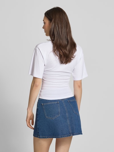 Frauenmodel trägt T-Shirt in tailliertem Schnitt Modell 'ELORA' von JJXX, weiß, Baumwoll-Mix, kombiniert mit Jeansrock, Ganzkörperansicht Rückansicht.
