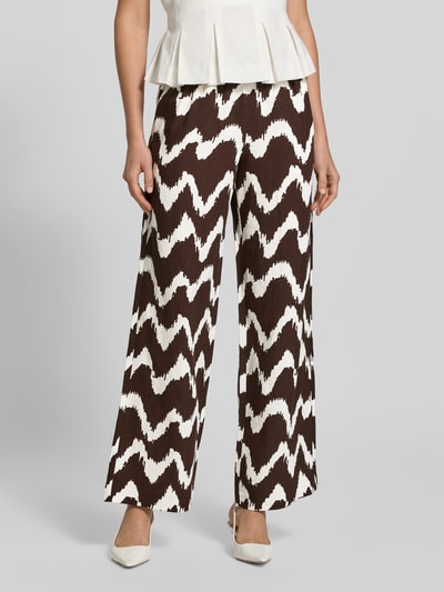 Kobiece modelka nosi spodnie z szerokimi nogawkami Wide Leg Pants aus Viskose-Mix mit elastischem Bund od OPUS PANTS, mieszanka wiskozy z lnem, krój loose fit, model 'Malotta', szerokość w rozmiarze 36: 37 cm, długość wewnętrzna nogawki w rozmiarze 36: 79 cm, wzór w zygzaki w kolorze brązowym i kremowym, tekstura lekko fakturowana, widok całej sylwetki z przodu.