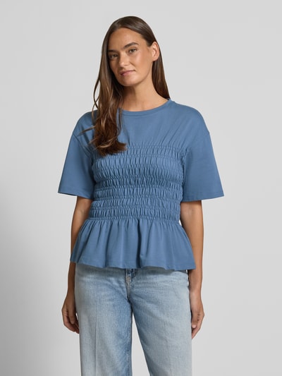 Modelka nosi T-Shirt mit Smok-Details und Rundhalsausschnitt von Jake*s Casual w kolorze niebieskim, czysta bawełna, krój slim fit, smokowane detale, okrągły dekolt, długość tyłu w rozmiarze S: 54 cm, widok całej sylwetki z przodu.