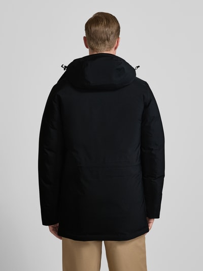 Männermodel draagt Parka met capuchon en klepzakken van PEAK PERFORMANCE, regular fit, ruglengte maat M 87 cm, schouderbreedte 47 cm, borstwijdte 59 cm, mouwlengte 73 cm, effen zwart, stevige stof, Ganzkörperansicht Rückansicht.