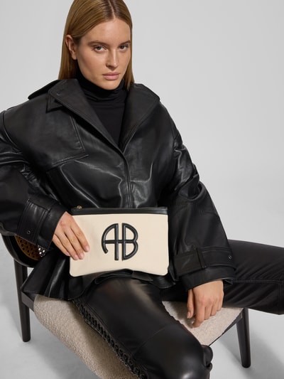 Frauenmodel trägt Pouch mit Logo-Detail von Anine Bing in Beige mit schwarzem Strukturmuster und kontrastivem Besatz, Nahaufnahme Oberkörper.